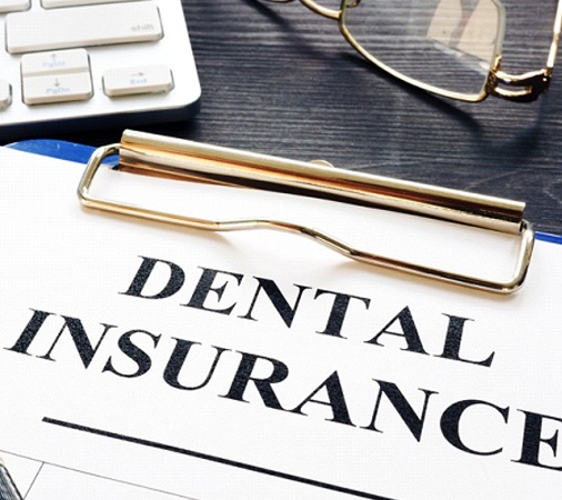 Dental insurance paperwork with computer, pen, and glasses
