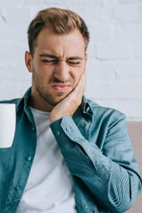 A young man with a coffee cup who’s suffering a toothache