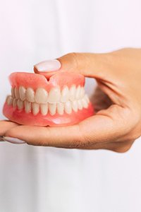 A person holding a set of full dentures in their hand