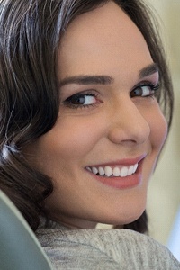 A young woman with her head turned and smiling as the dentist looks on in preparation for treatment